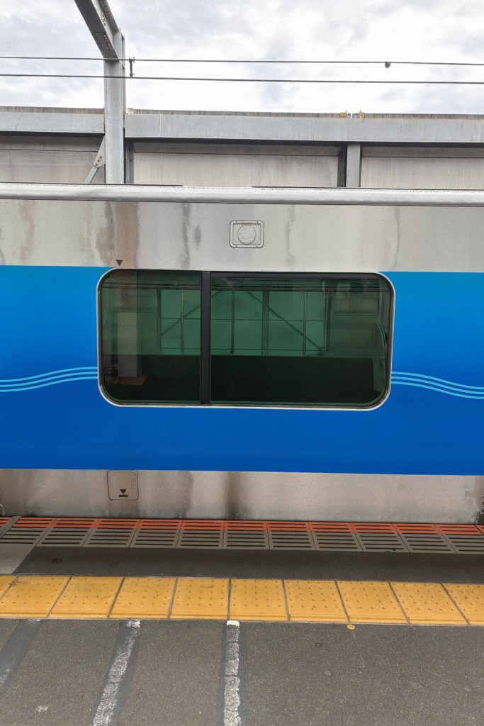A close-up view of a blue and silver train car door, partially open, showcasing a green-tinted window and the platform below.